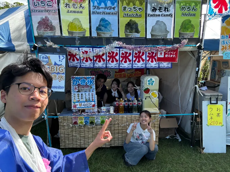 Pann taking a selfie in front of the team's shaved-ice stall, with teammates behind the counter