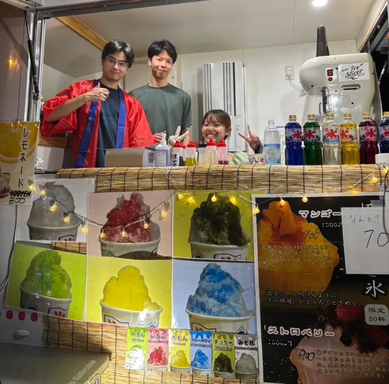 The food truck window: Pann and two teammates behind the counter, the photo menu of every flavour, and premium mango and strawberry posters with crossed-out prices and a limit of 50 cups